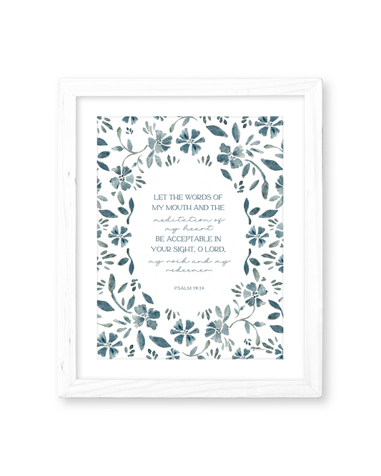 A framed wall art print featuring a botanical floral border in muted blue-gray tones around a central Bible verse from Psalm 19:14. The print is mounted in a white rectangular frame against a clean white background.