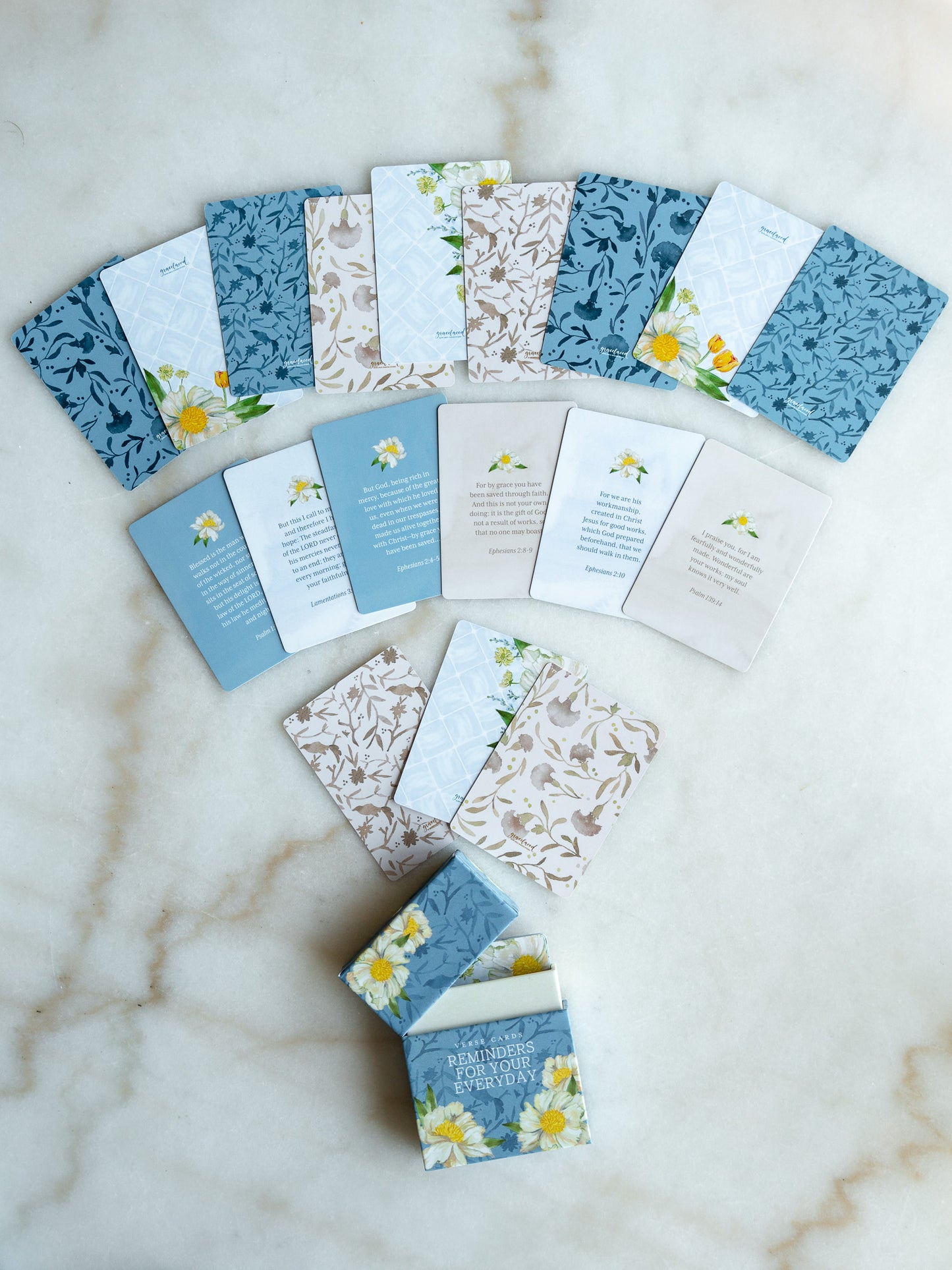 A coordinated set of small printed cards or envelopes arranged on a light marble surface. The pieces feature blue floral and botanical patterns, white sections, beige botanical prints, and small yellow flower illustrations.